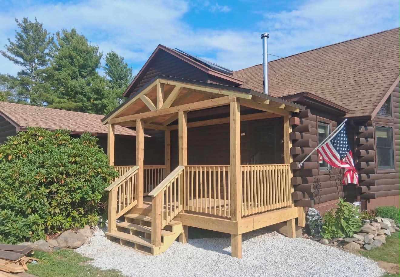 Completed covered porch addition on log cabin with American flag